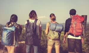 Four hikers with backpacks stand together, gazing at a scenic mountain view under a clear sky.