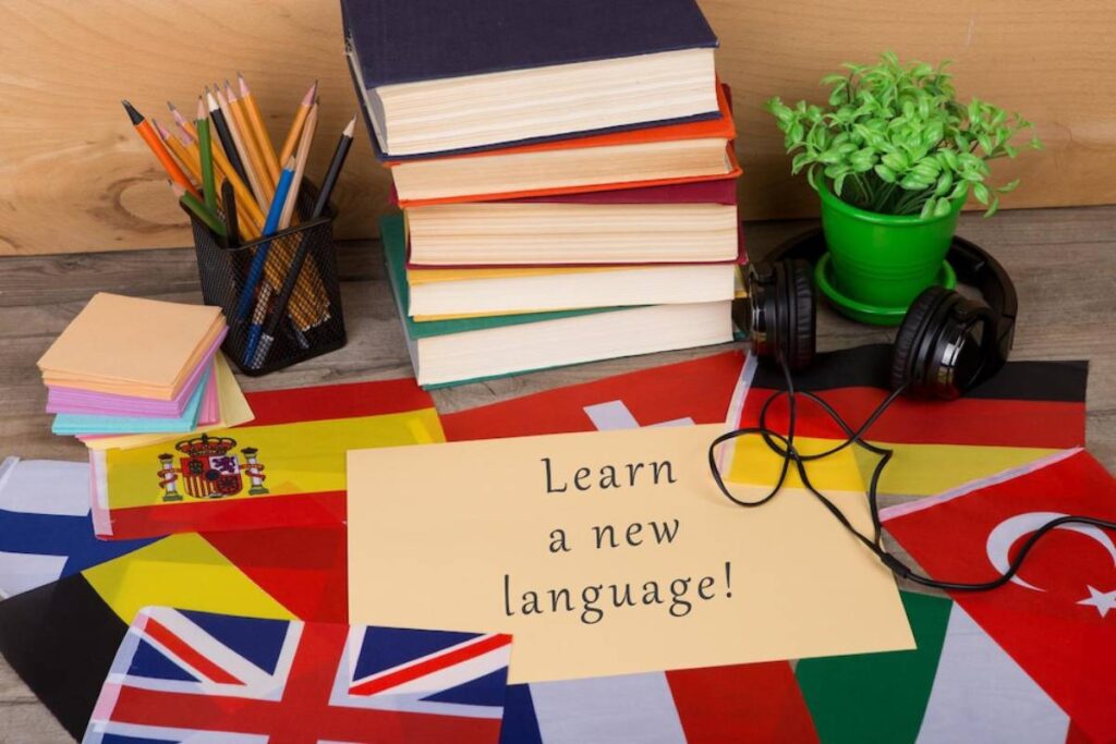 A study setup featuring colorful flags, books, sticky notes, headphones, and a sign reading Learn a new language!