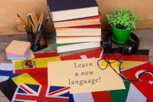 A study setup featuring colorful flags, books, sticky notes, headphones, and a sign reading Learn a new language!
