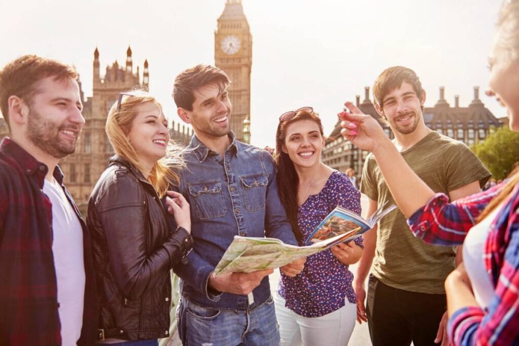 A group of six friends gathered outdoors, examining a map with Big Ben in the background during a sunny day.