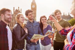 A group of six friends gathered outdoors, examining a map with Big Ben in the background during a sunny day.