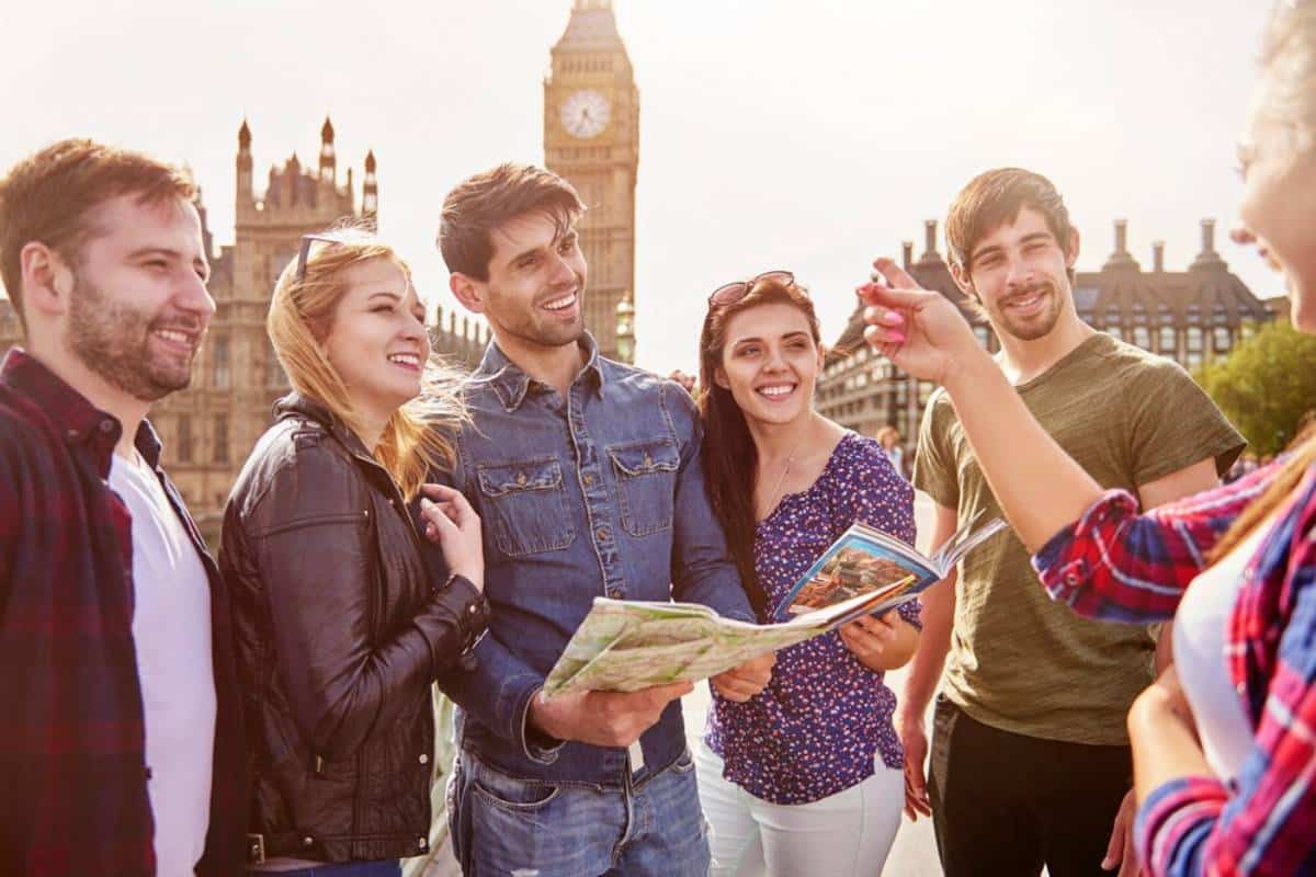 A group of six friends gathered outdoors, examining a map with Big Ben in the background during a sunny day.