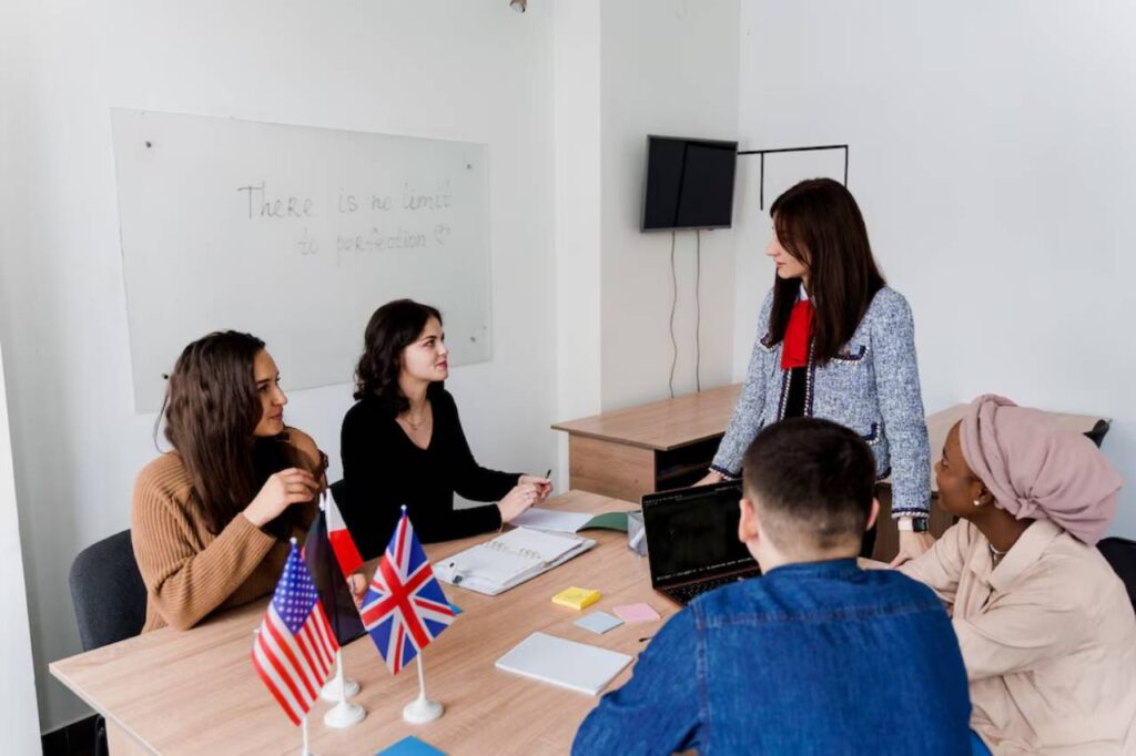 A group of professionals engaged in a discussion around a conference table with notebooks, laptops, and national flags displayed.
