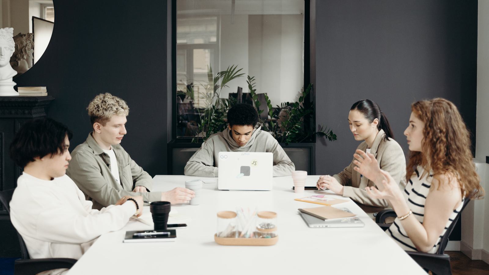  A diverse group of professionals engaged in a meeting around a modern conference table, surrounded by greenery and stylish decor.