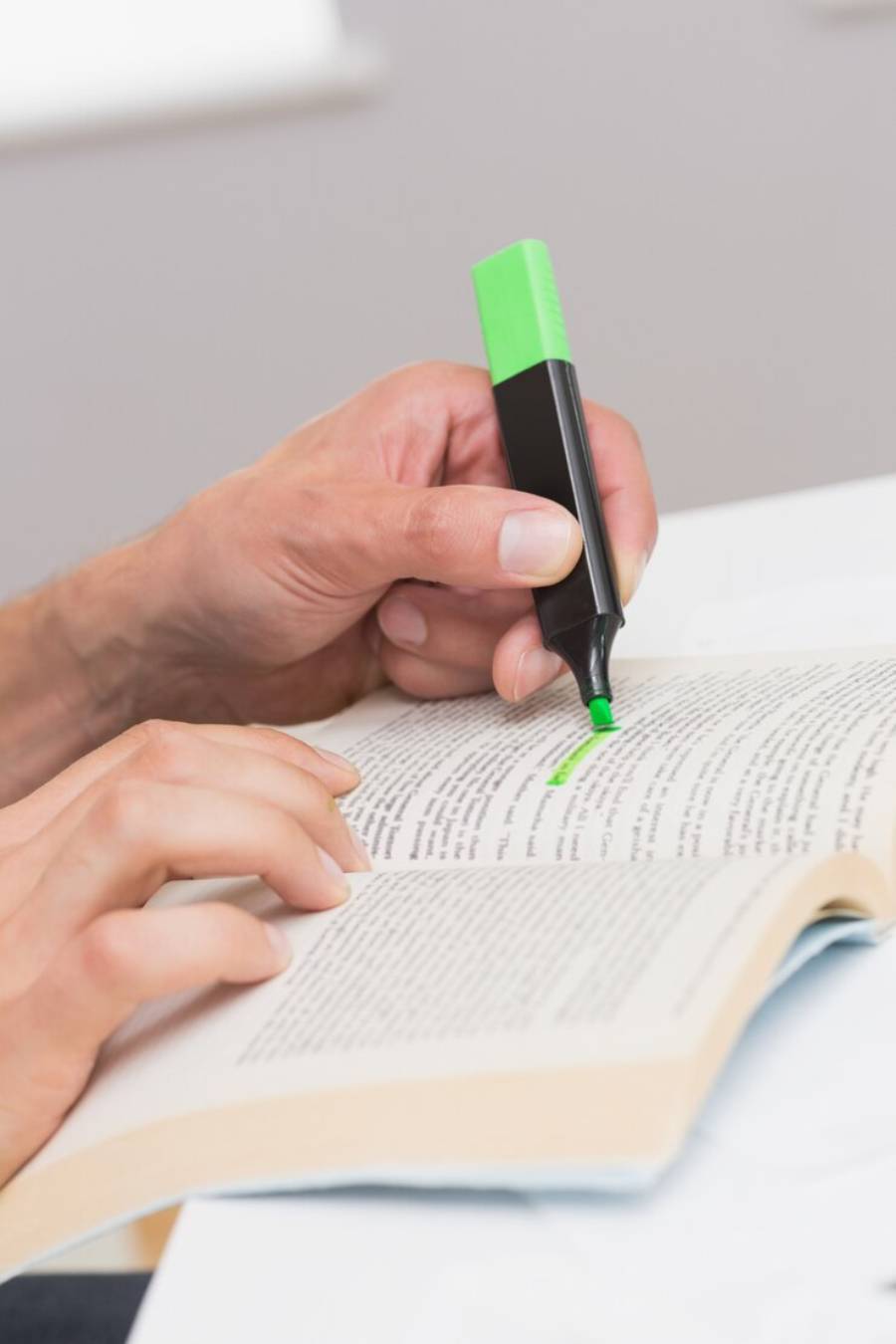  A person highlighting text in a book with a green highlighter, focused on the written content.