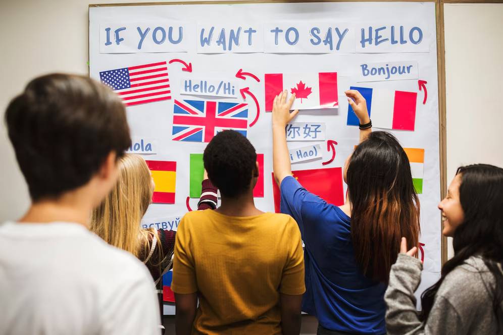  A group of people interacts with a poster displaying various flags and greetings in different languages, including 
