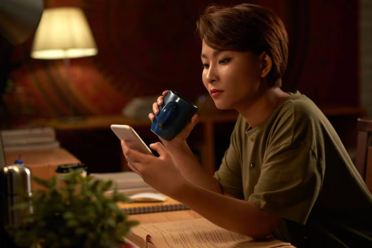  . A woman sitting at a table, focused on her phone, with a relaxed expression.